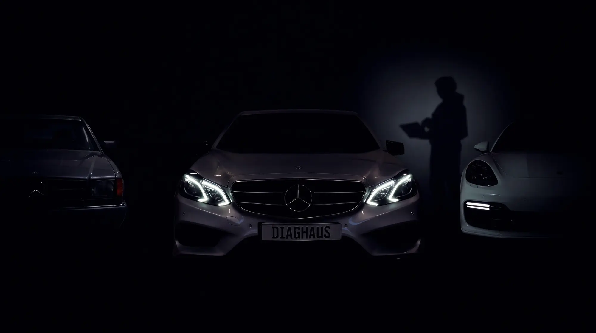 Kolme autoa DiagHausin korjaamolla, keskella Mercedes-Benz E-sarja ajovalot paalla